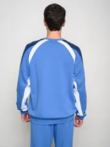 Buzo deportivo de manga larga, color principal rojo, con mangas azul marino y detalles en blanco que bajan desde el hombro hasta el puño. Presenta cuello redondo, logo Umbro y escudo del Club Nacional de Football en el pecho.