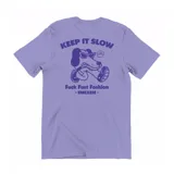 Remera de algodón color lila con estampa gráfica en la espalda que incluye un perro con lentes de sol y el texto 'Keep It Slow - Fuck Fast Fashion'.