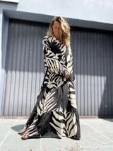 Vestido largo tipo túnica con estampado de hojas en contraste blanco y negro. Presenta cuello camisero con botones, mangas largas amplias y falda con volados escalonados.