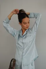 Pijama de satén elastizado color celeste, compuesto por una camisa de manga larga con cuello solapa, botones frontales y bolsillo en el pecho, y un pantalón recto con cintura elástica y lazo ajustable.