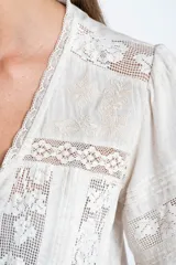 Blusa color crudo de manga corta abullonada, con escote en V y detalles de encaje y bordados verticales en el frente y mangas.