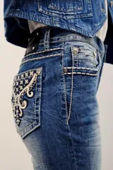 Pantalón jean de corte chupín, tiro medio y lavado azul con efecto gastado. Cuenta con bolsillos traseros con bordados ornamentales y tachas metálicas.