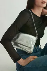 Cartera tipo bandolera de cuero metalizado plateado, con solapa frontal y logo de la marca grabado. Incluye una correa combinada de cadena metálica y cuero, desmontable y regulable.