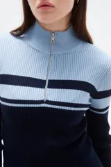 Polera de punto acanalado con diseño bicolor en blanco y negro, cuello alto con cierre frontal y manga larga.