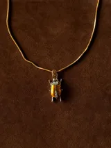 Collar de cadena fina dorada con dije en forma de escarabajo esmaltado en color dorado con detalles de cristales incrustados.