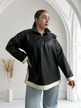 Buzo negro de ecocuero con cuello polo, cierre frontal con cremallera dorada y puños con elástico.