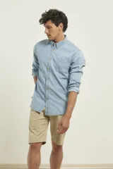 Camisa de hombre de denim azul, manga larga, con cuello buttondown y un bolsillo de parche en el pecho izquierdo.