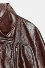 Chaqueta de corte amplio estilo biker en tejido efecto piel de color verde oscuro, con cuello alto envolvente, cierre frontal asimétrico de cremallera metálica, bolsillos ocultos en costura y forro interior.