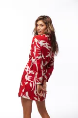 Vestido corto tipo camisero color rojo con estampado de hojas blancas, cuello camisero, cierre frontal con botones, mangas largas y elástico en la cintura.
