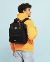 Mochila Cabaia modelo Adventurer en color negro, confeccionada en tejido de pana con base y detalles en cuero sintético. Cuenta con asas superiores, bolsillo frontal con cierre y parches de marca en tono cuero.