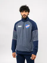 Buzo deportivo de medio cierre marca Umbro del Club Nacional de Football. Presenta un diseño en tonos azul y gris jaspeado, con cuello alto, mangas largas y detalles de costuras en contraste. Incluye el escudo del club y logo de la marca en el pecho.