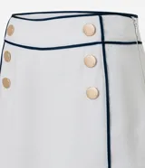 Short sastre de cintura alta confeccionado en crepé color blanco, con botones delanteros metalizados, cierre lateral por cremallera, bolsillos falsos atrás y bies contrastante en color negro.