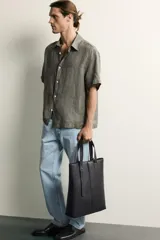 Jeans regular fit de mezclilla negra con efecto lavado, corte recto y tiro medio. Cuenta con diseño de cinco bolsillos y cierre frontal con cremallera y botón.