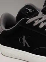 Zapatillas urbanas Calvin Klein Jeans de ante negro con logo CK grabado en el lateral, detalle de talón en gris, cordones grises y suela cupsole blanca.