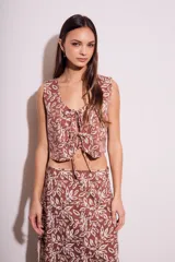 Chaleco marrón con estampado de hojas blancas, escote en V y lazos ajustables en el frente.