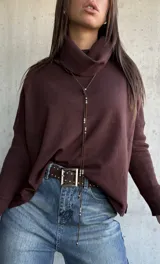 Sweater de tejido de punto color chocolate, con cuello polera, mangas largas con puños acanalados y diseño holgado con aberturas laterales y detalle de botones.