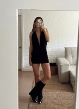 Vestido corto negro con escote halter profundo y diseño drapeado en la parte frontal y lateral. Confeccionado en tela elástica ajustada al cuerpo.