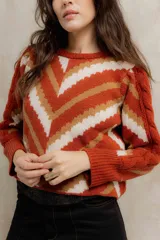 Sweater de punto jacquard con diseño de chevron en tonos celeste y marrón. Presenta cuello redondo, corte holgado y mangas largas con hombros abullonados.