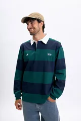Remera polo de manga larga a rayas horizontales en azul marino y verde oscuro, con cuello blanco y tapeta de botones. Incluye la estampa "1979" en el pecho.