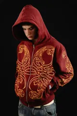 Hoodie con cierre frontal, color bordó, con estampado serigráfico en color dorado que recorre el frente y las mangas con un diseño inspirado en hojas de acanto. Cuenta con bolsillos laterales y cierre metálico.