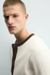 Camiseta de manga larga en tejido de punto canalé color crudo, con cuello redondo y tapeta frontal con botones en color marrón oscuro a contraste.