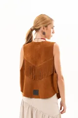 Chaleco de cuero descarne color tostado, con diseño oversize y terminación en picos. Presenta tachas metálicas a lo largo de la abertura frontal y flecos en la espalda.