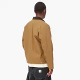 Chaqueta Carhartt modelo Detroit, color tostado, con cuello de pana en contraste, cierre frontal con cremallera, bolsillo en el pecho con cremallera y logo de la marca bordado.