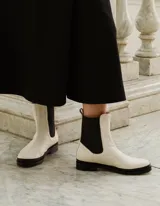 Bota Chelsea color hueso de cuero vacuno, con elástico lateral negro y suela de cuero.