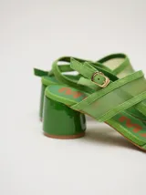 Sandalias de taco redondo de 6 cm, confeccionadas en gamuza verde con tiras frontales y de tobillo en material translúcido. Cuentan con cierre de pulsera al tobillo y plantilla de cuero.