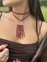Gargantilla de cuero trenzado color bordó con dije de flecos de cuero bordó con cuentas plateadas y aro metálico plateado.