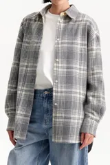 Camisa de tejido grueso con patrón de cuadros en tonos gris y blanco, de corte amplio y cierre frontal abotonado.