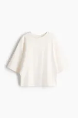 Remera oversized en tejido de felpa liviano color blanco, con mangas anchas al codo y cuello redondo ribeteado.