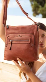 Bandolera de símil cuero color marrón, con diseño de doble bolsillo frontal con cierre y detalles de tachas metálicas. Cuenta con correa larga regulable, bolsillo trasero con cierre y compartimentos internos.