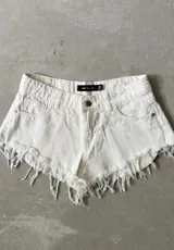 Short de jean color blanco off-white, de tiro medio, con bolsillos clásicos y terminación desmechada con flecos en el ruedo.