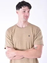 Remera de manga corta con textura de rayas horizontales en relieve, cuello redondo y pequeño aplique metálico en el pecho.