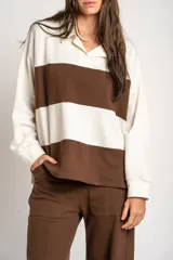 Sweater de tejido de punto con diseño a rayas horizontales en color crema y marrón. Presenta cuello tipo polo con cierre frontal de botones ocultos, mangas largas y un corte oversize.
