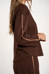 Sweater de manga larga color café, con textura gofrada y cuello redondo. Presenta una fina línea decorativa de color beige en el exterior de ambas mangas.