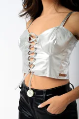 Corset plateado de cuero sintético con tirantes finos y ajuste frontal con cordones.