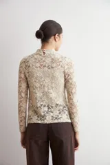 Media polera de encaje color beige con diseño floral, cuello alto y mangas largas.