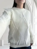 Sweater blanco de tejido de punto con cuello redondo y mangas largas. Presenta un diseño con rombos y flecos.