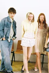 Vestido corto color crema/hueso, con escote recto y tirantes finos cruzados en la espalda. Presenta paneles de encaje en el centro del busto y a los lados de la cintura. La falda es fluida con godets y bajo asimétrico.