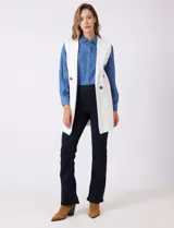 Chaleco largo tejido color blanco de la marca Sioni, con cuello solapa, doble botonadura dorada en el frente y bolsillos aplicados.