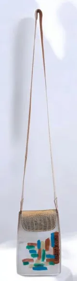 Bandolera compacta de cuero color blanco, con solapa de cuero texturizado metalizado dorado y diseño pintado a mano en el frente. Cuenta con cierre de broche imán y correa larga de cinta textil con detalles en cuero grabado.