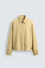 Cazadora regular fit de color beige, confeccionada en mezcla de algodón y lyocell. Cuenta con cuello camisero, cierre frontal de cremallera, bolsillos de plastrón en la cadera, mangas largas con puños elásticos y bajo con ajuste elástico.