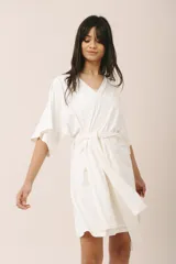 Bata corta color crema, confeccionada en algodón con elastano, con escote en V, mangas anchas y lazo para ajustar en la cintura.