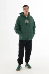 Buzo hoodie verde oscuro con estampa serigráfica frontal de alta definición con una escena urbana en estilo puntillista y logo VERNAL con efecto dorado envejecido. Corte oversize con hombros caídos, capucha doble y bolsillo canguro.