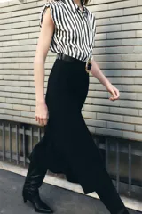 Vestido midi de diseño combinado con cuerpo de camisa sin mangas a rayas verticales en blanco y negro, y falda negra de corte recto. Presenta cuello solapa, cierre frontal con botones y cinturón negro con hebilla metálica dorada.
