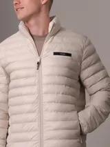 Campera acolchada color beige claro, con cuello alto y cierre frontal con cremallera. Tiene bolsillos laterales y logo de Calvin Klein en el pecho.