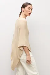 Capa tejida en hilo de lurex color beige, con cuello bote y diseño asimétrico de corte fluido.