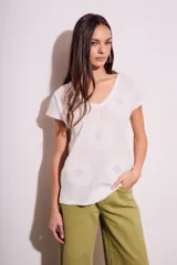 Remera de algodón color blanco con cuello en V y mangas cortas. Presenta un diseño con flores bordadas en relieve y detalles calados en el tejido.